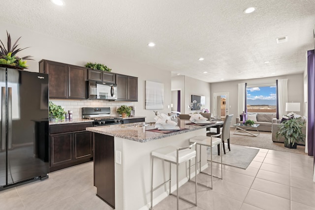 kitchen with black appliances, light tile patterned floors, open floor plan, a breakfast bar, and a textured ceiling