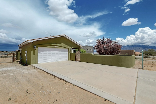 5721 Miller Rd NE, Rio Rancho, NM 87144 - view of property exterior featuring fence, stucco siding, driveway, a garage, and a mountain view