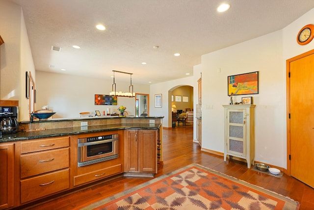 6119 La Paz Rd NE, Rio Rancho, NM 87144 - kitchen with dark wood-style floors, arched walkways, brown cabinets, stainless steel oven, and a peninsula