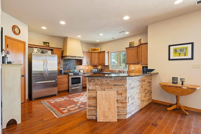 6119 La Paz Rd NE, Rio Rancho, NM 87144 - kitchen featuring appliances with stainless steel finishes, custom exhaust hood, brown cabinets, dark wood finished floors, and dark countertops