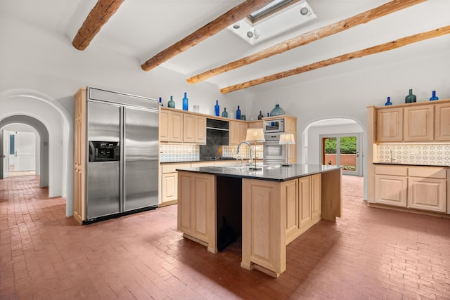 384 Chaparral Ln, Corrales, NM 87048 - kitchen featuring built in appliances, arched walkways, tasteful backsplash, beam ceiling, and a kitchen island with sink
