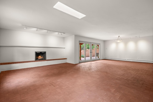 384 Chaparral Ln, Corrales, NM 87048 - unfurnished living room featuring a baseboard heating unit, rail lighting, a warm lit fireplace, and brick floors
