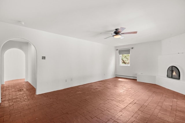 384 Chaparral Ln, Corrales, NM 87048 - unfurnished living room with brick patterned flooring, a baseboard radiator, ceiling fan, arched walkways, and a warm lit fireplace