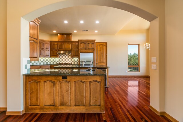 9 Canon Escondido, Sandia Park, NM 87047 - kitchen with arched walkways, under cabinet range hood, dark wood-style floors, dark stone countertops, and tasteful backsplash
