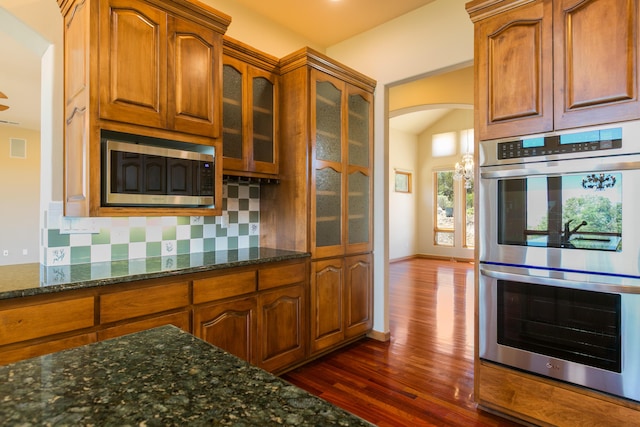 9 Canon Escondido, Sandia Park, NM 87047 - kitchen featuring appliances with stainless steel finishes, arched walkways, dark wood-style flooring, brown cabinetry, and dark stone counters