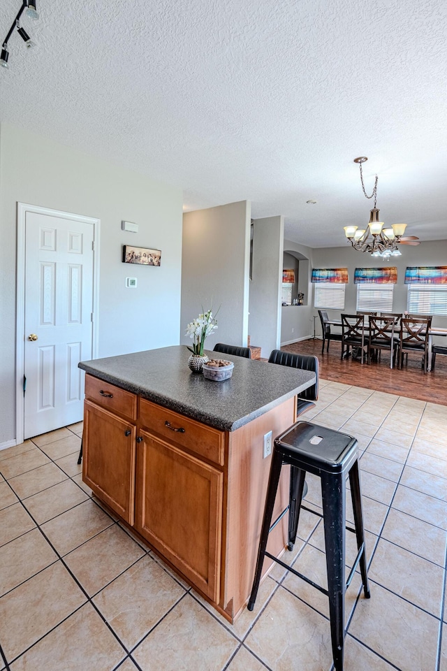 10500 Trieste Ct NW, Albuquerque, NM 87114 - kitchen featuring dark countertops, light tile patterned floors, a center island, a textured ceiling, and a chandelier