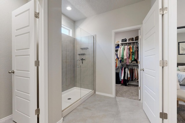 3179 Kunzita St SE, Rio Rancho, NM 87124 - ensuite bathroom with a shower stall, a spacious closet, a textured ceiling, baseboards, and tile patterned floors