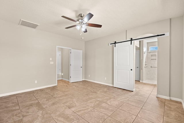 4909 Calle Espana NW, Albuquerque, NM 87120 - unfurnished bedroom with a barn door, ensuite bathroom, a textured ceiling, ceiling fan, and baseboards