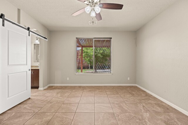 4909 Calle Espana NW, Albuquerque, NM 87120 - unfurnished bedroom featuring a barn door, a textured ceiling, ceiling fan, ensuite bathroom, and baseboards