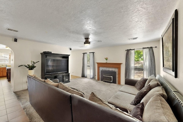 6242 Roadrunner Loop NE, Rio Rancho, NM 87144 - living room with arched walkways, a ceiling fan, a tiled fireplace, a textured ceiling, and light tile patterned flooring
