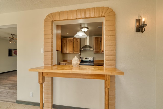 508 Las Marias Dr SE, Rio Rancho, NM 87124 - kitchen featuring wall chimney range hood, stainless steel electric range oven, butcher block countertops, a ceiling fan, and a peninsula