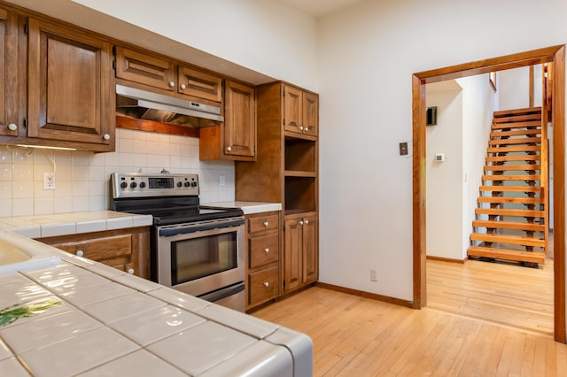 3121 Grande Vista Pl NW, Albuquerque, NM 87120 - kitchen with under cabinet range hood, stainless steel range with electric cooktop, tile countertops, light wood-style flooring, and decorative backsplash