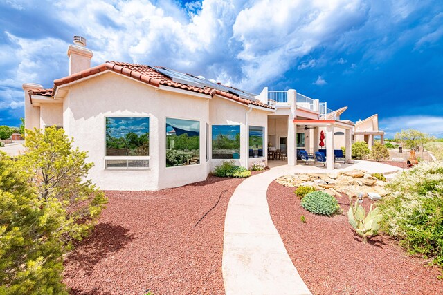 2392 Manzano Loop NE, Rio Rancho, NM 87144 - back of house with a chimney, roof mounted solar panels, stucco siding, a patio area, and ceiling fan