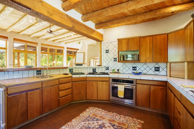59 Perdiz Canyon Rd, Placitas, NM 87043 - kitchen with appliances with stainless steel finishes, a sink, wooden ceiling with exposed beams, brick flooring, and backsplash