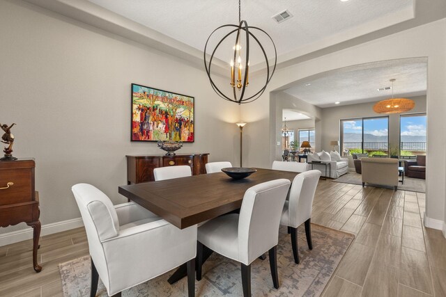 6808 Vista Luces St NW, Albuquerque, NM 87120 - dining space with arched walkways, a chandelier, light wood-style flooring, baseboards, and a textured ceiling