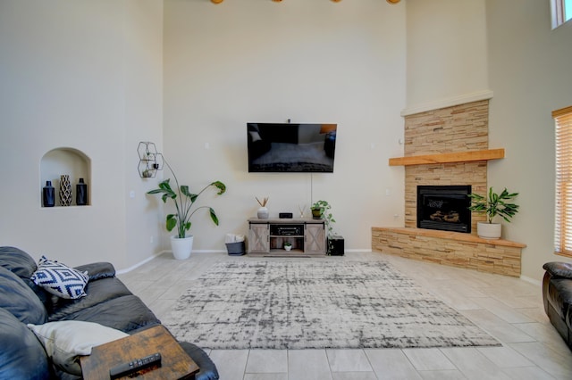 living area featuring a towering ceiling, a stone fireplace, tile patterned flooring, and baseboards