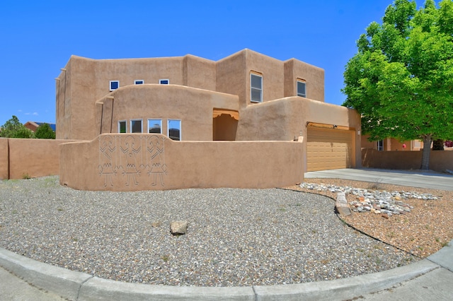 adobe home with fence, stucco siding, an attached garage, and driveway