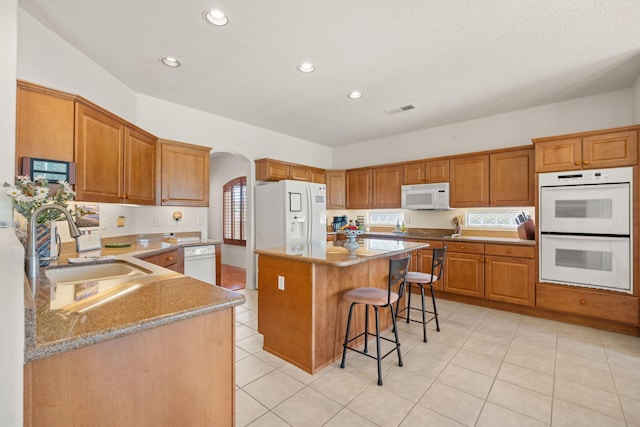 3916 Alamogordo Dr NW, Albuquerque, NM 87120 - kitchen with white appliances, a sink, arched walkways, a kitchen bar, and light stone counters