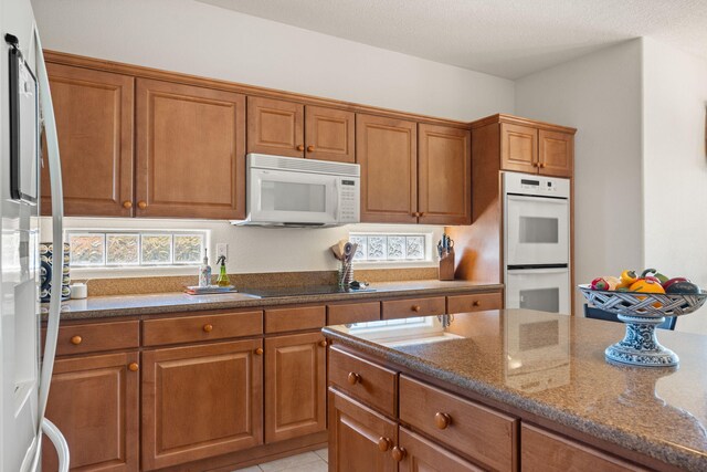 3916 Alamogordo Dr NW, Albuquerque, NM 87120 - kitchen featuring white appliances, brown cabinets, dark stone counters, and light tile patterned floors