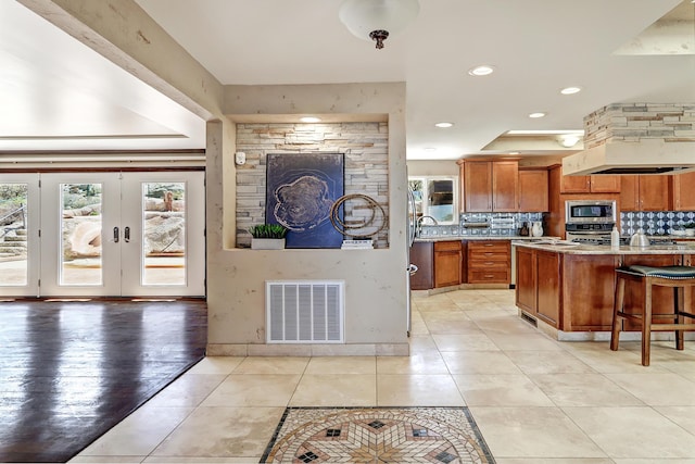 1106 Warm Sands Dr SE, Albuquerque, NM 87123 - kitchen featuring stainless steel appliances, brown cabinetry, backsplash, light tile patterned floors, and a kitchen bar