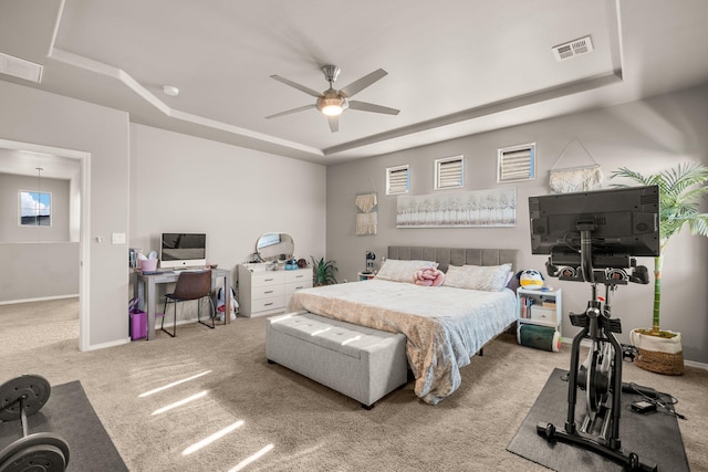 carpeted bedroom with a raised ceiling, an office area, baseboards, and a ceiling fan