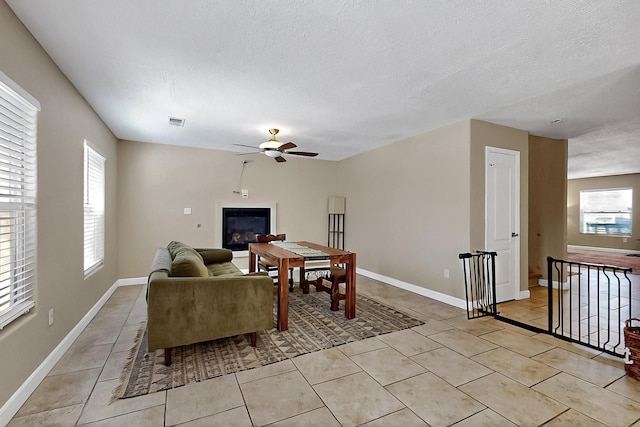 5727 Cibola Dr NE, Rio Rancho, NM 87144 - living room featuring a ceiling fan, light tile patterned floors, a glass covered fireplace, and a textured ceiling