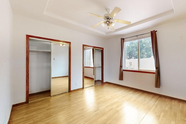 13401 Blue Flax Ct NE, Albuquerque, NM 87111 - unfurnished bedroom featuring a tray ceiling, multiple closets, light wood-type flooring, and baseboards