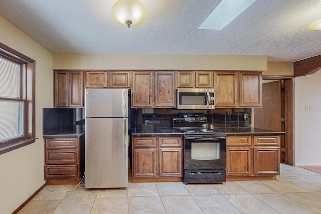 501 Calle De La Angel, Bernalillo, NM 87004 - kitchen featuring appliances with stainless steel finishes, dark countertops, brown cabinetry, a textured ceiling, and decorative backsplash