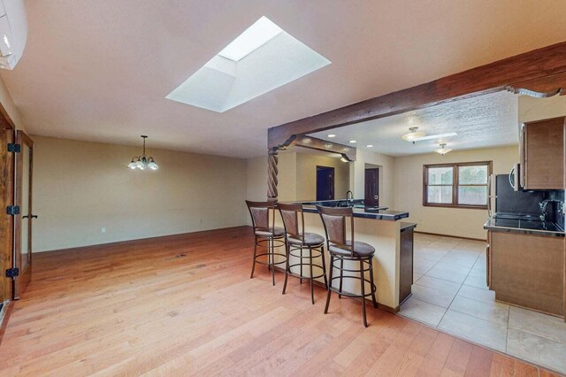 501 Calle De La Angel, Bernalillo, NM 87004 - kitchen with a breakfast bar area, dark countertops, light wood-type flooring, a skylight, and a chandelier