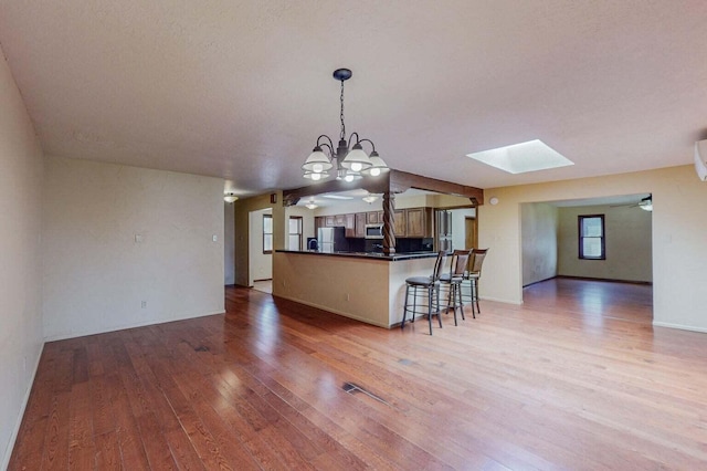 501 Calle De La Angel, Bernalillo, NM 87004 - kitchen with freestanding refrigerator, dark countertops, light wood finished floors, a skylight, and a breakfast bar area
