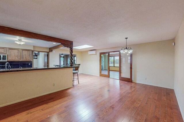501 Calle De La Angel, Bernalillo, NM 87004 - unfurnished living room with light wood-type flooring, a textured ceiling, a chandelier, beamed ceiling, and an AC wall unit