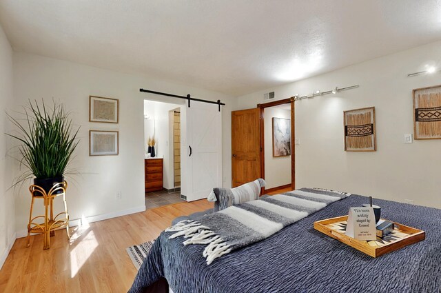 9737 Academy St NW, Albuquerque, NM 87114 - bedroom featuring a barn door, light wood-type flooring, baseboards, and connected bathroom