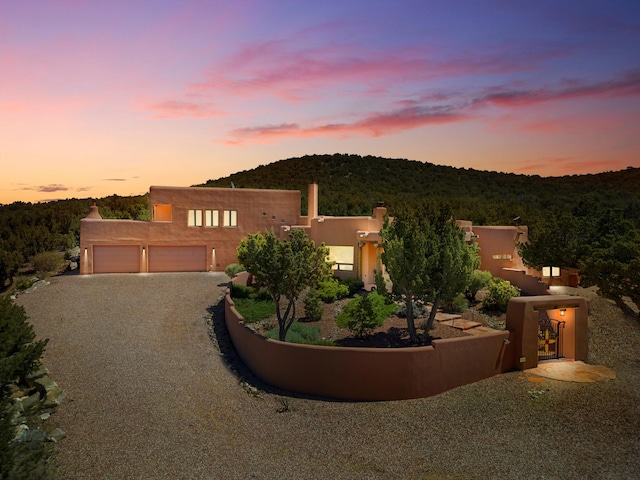 28 Canon Escondido, Sandia Park, NM 87047 - pueblo-style house featuring stucco siding, gravel driveway, a garage, and a forest view