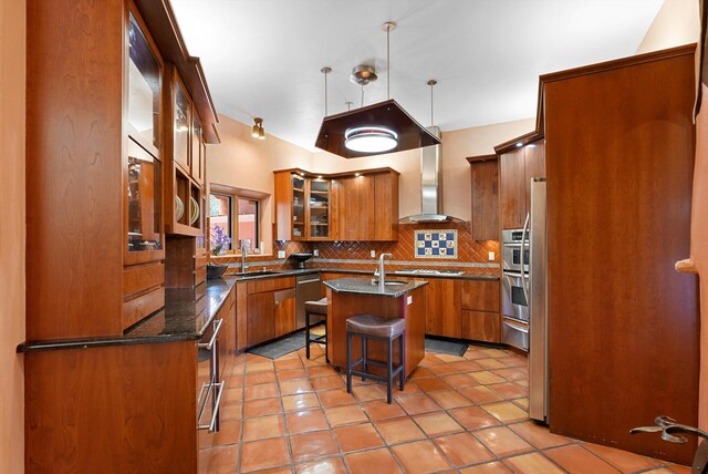28 Canon Escondido, Sandia Park, NM 87047 - kitchen with brown cabinetry, wall chimney range hood, a sink, a center island with sink, and tasteful backsplash