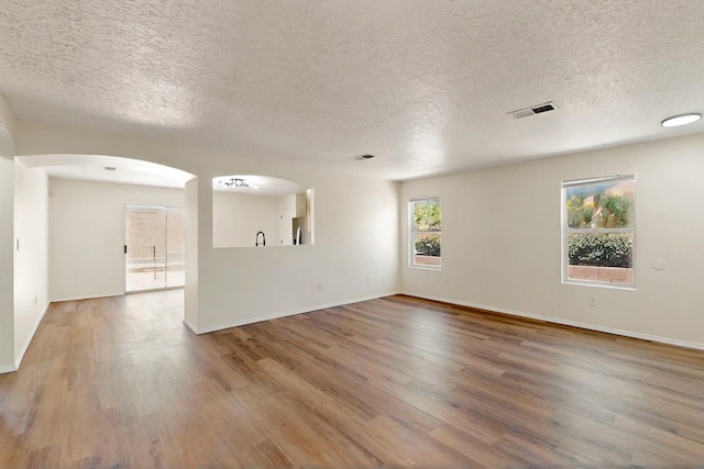 9927 Silverton Dr NW, Albuquerque, NM 87114 - empty room featuring wood finished floors, a textured ceiling, arched walkways, and baseboards