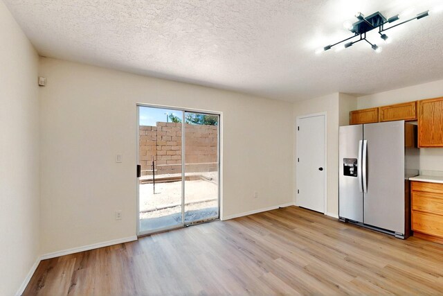 9927 Silverton Dr NW, Albuquerque, NM 87114 - kitchen with stainless steel fridge, light wood-type flooring, a textured ceiling, brown cabinets, and baseboards