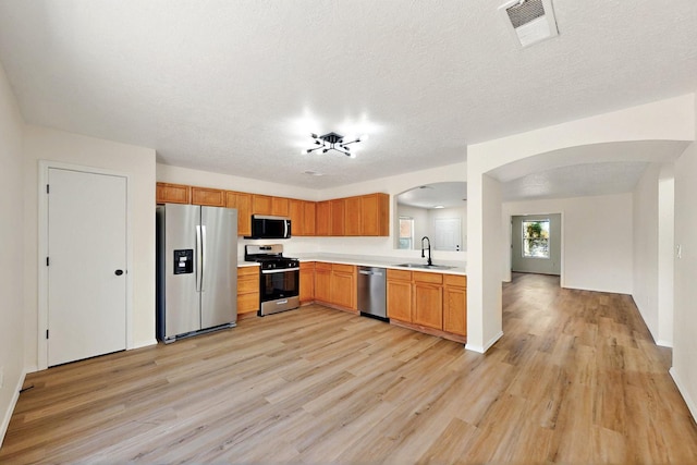 9927 Silverton Dr NW, Albuquerque, NM 87114 - kitchen featuring stainless steel appliances, arched walkways, a sink, light wood-type flooring, and light countertops