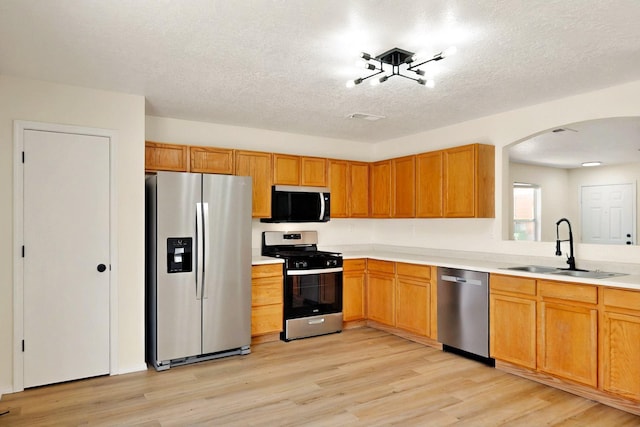 9927 Silverton Dr NW, Albuquerque, NM 87114 - kitchen with appliances with stainless steel finishes, a sink, arched walkways, light wood-style floors, and light countertops