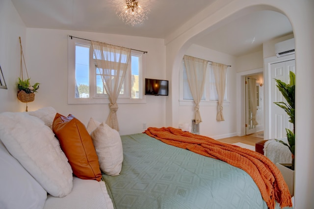 223 14th St NW, Albuquerque, NM 87104 - bedroom featuring a wall unit AC, arched walkways, a chandelier, and wood finished floors