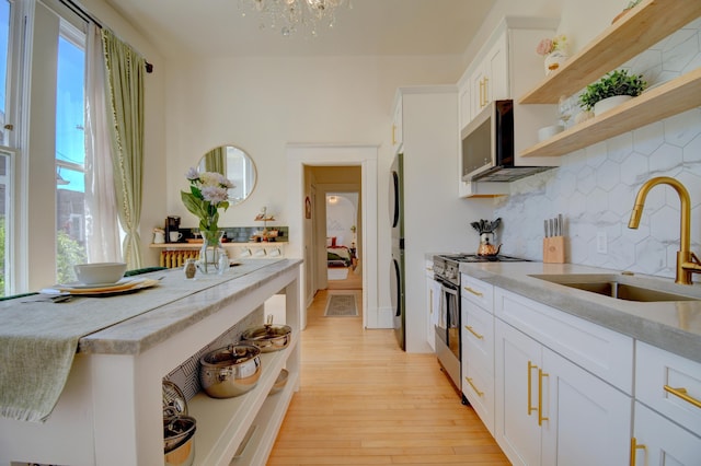 223 14th St NW, Albuquerque, NM 87104 - kitchen featuring appliances with stainless steel finishes, stacked washing machine and dryer, a sink, open shelves, and backsplash