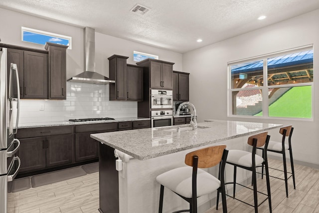 1661 Camino Culiacan, Los Lunas, NM 87031 - kitchen with wall chimney exhaust hood, stainless steel appliances, a sink, wood finish floors, and a textured ceiling