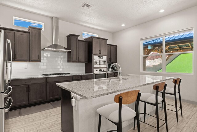1661 Camino Culiacan, Los Lunas, NM 87031 - kitchen with wall chimney exhaust hood, appliances with stainless steel finishes, wood tiled floors, a sink, and a textured ceiling