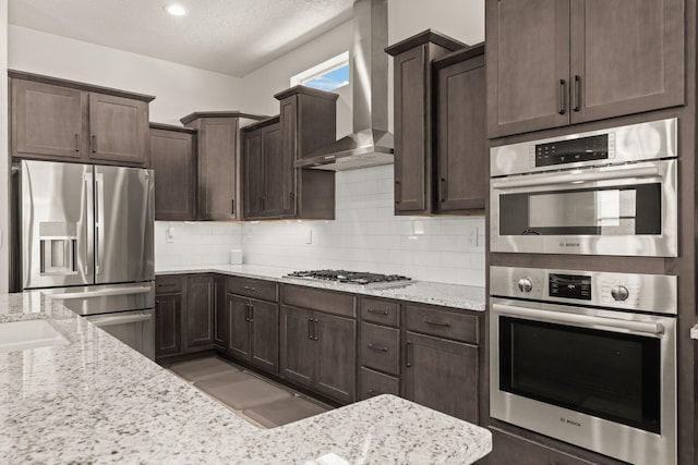 1661 Camino Culiacan, Los Lunas, NM 87031 - kitchen featuring stainless steel appliances, wall chimney range hood, dark brown cabinetry, tasteful backsplash, and a textured ceiling