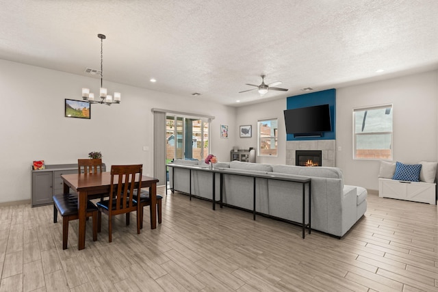 1661 Camino Culiacan, Los Lunas, NM 87031 - dining area with a textured ceiling, a ceiling fan, light wood-style floors, a tile fireplace, and a chandelier
