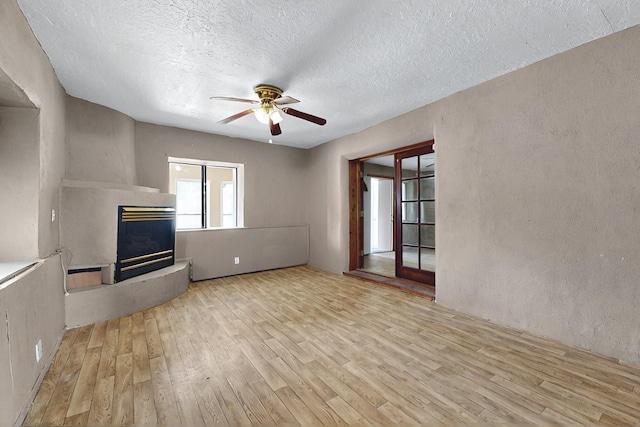 1237 Gabaldon Rd, Belen, NM 87002 - unfurnished living room with wood finished floors, a ceiling fan, a glass covered fireplace, and a textured ceiling
