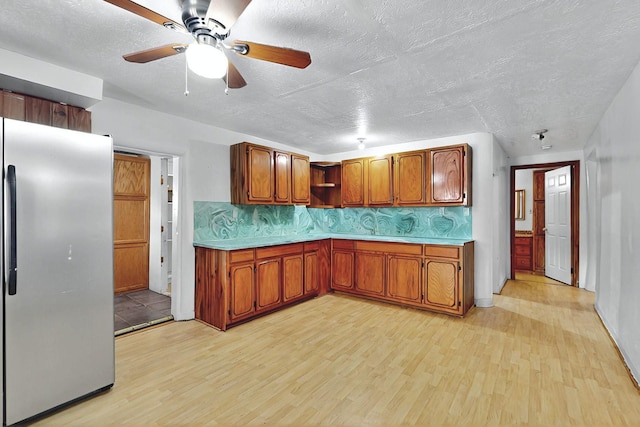 1237 Gabaldon Rd, Belen, NM 87002 - kitchen featuring freestanding refrigerator, light wood-style floors, ceiling fan, brown cabinetry, and a textured ceiling
