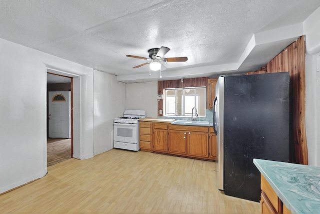 1237 Gabaldon Rd, Belen, NM 87002 - kitchen featuring white gas stove, freestanding refrigerator, a sink, light wood-style floors, and brown cabinets