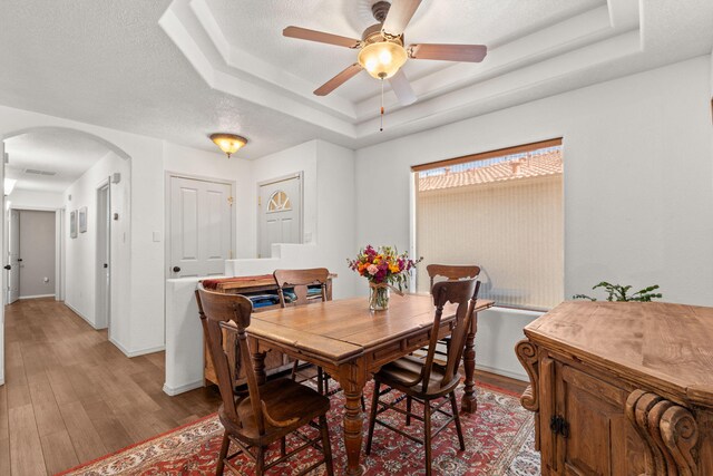3827 Fox Sparrow Trl NW, Albuquerque, NM 87120 - dining room featuring a raised ceiling, arched walkways, light wood-type flooring, ceiling fan, and baseboards