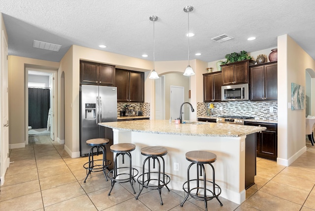 2659 Vista Manzano Loop NE, Rio Rancho, NM 87144 - kitchen with appliances with stainless steel finishes, a sink, dark brown cabinetry, light tile patterned flooring, and a center island with sink