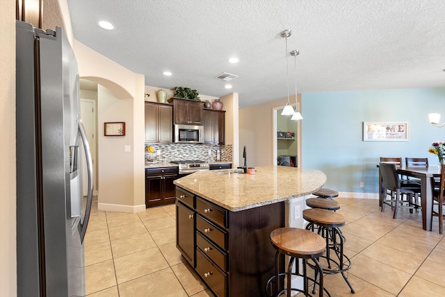 2659 Vista Manzano Loop NE, Rio Rancho, NM 87144 - kitchen with appliances with stainless steel finishes, a breakfast bar, arched walkways, light tile patterned floors, and a kitchen island with sink